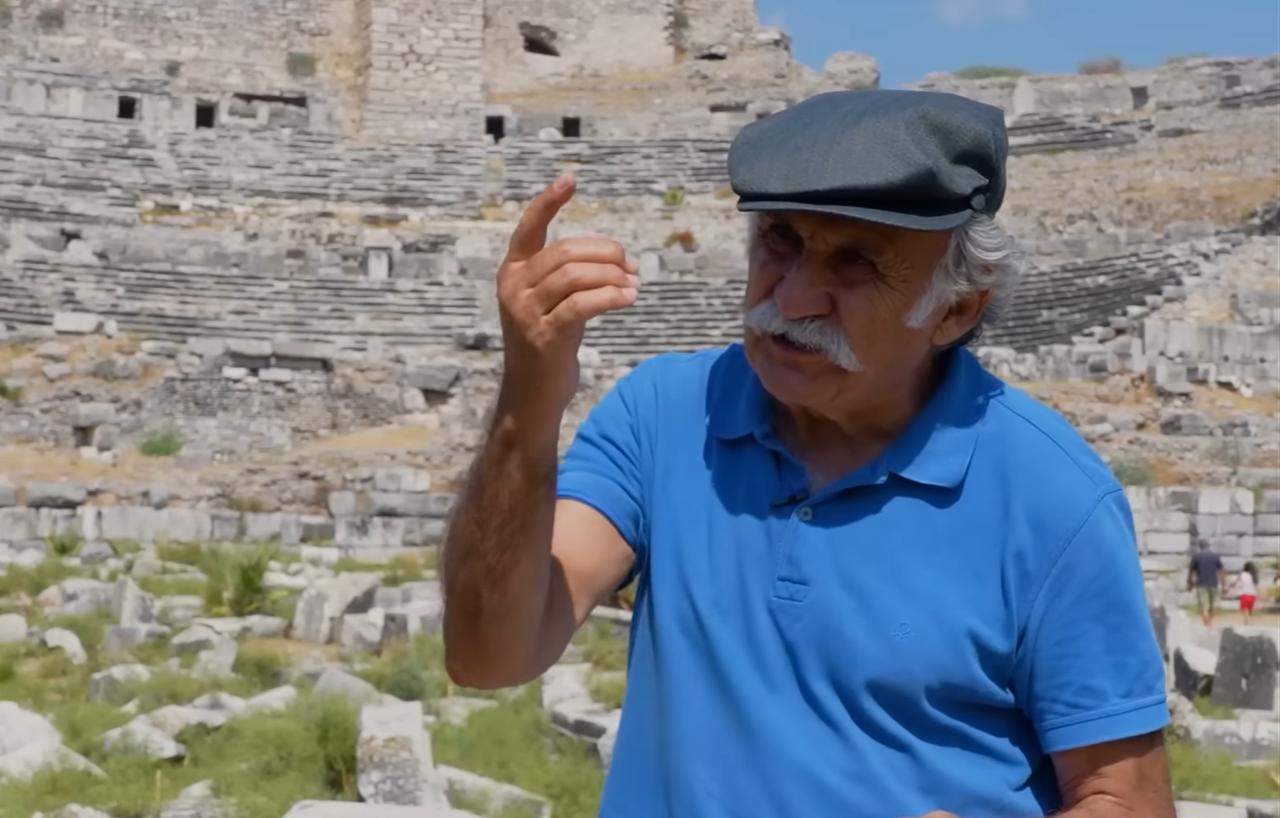 Professor Fahri Isik gestures while explaining the ancient theater of Patara, one of Türkiye’s key archaeological sites. (Photo via YouTube/@issanat)