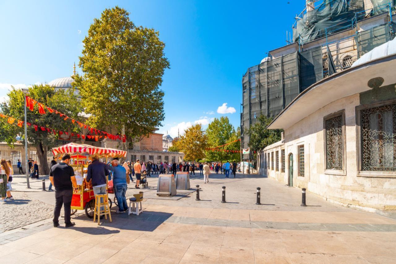 People gather around a street vendor in front of a mosque under renovation in Eminonu district of Istanbul, Türkiye. (Adobe Stock Photo)