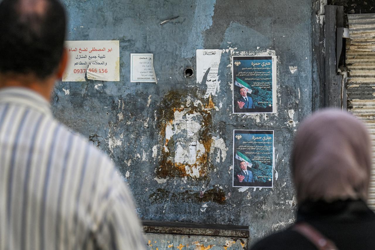 People view election posters of  Henry Hamra, a Syrian-American parliamentary candidate who is the first Jewish representative in the Syrian parliament since the late 1940s, displayed on a wall along an alley in the Jewish quarter of the old city of Damascus on October 3, 2025 .( AFP Photo )