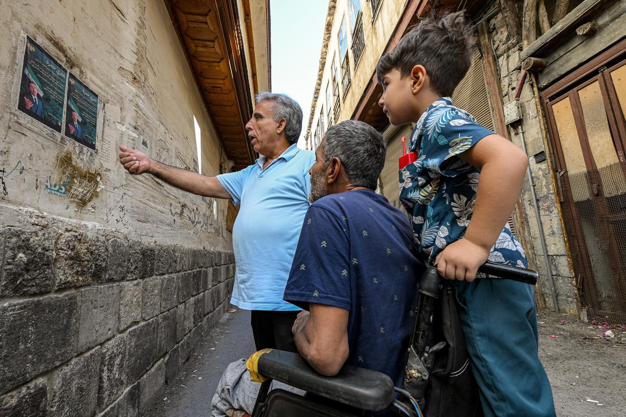 People view election posters of Henry Hamra, a Syrian-American parliamentary candidate  displayed on a wall along an alley in the Jewish quarter of the old city of Damascus on October 3, 2025 .(AFP Photo)