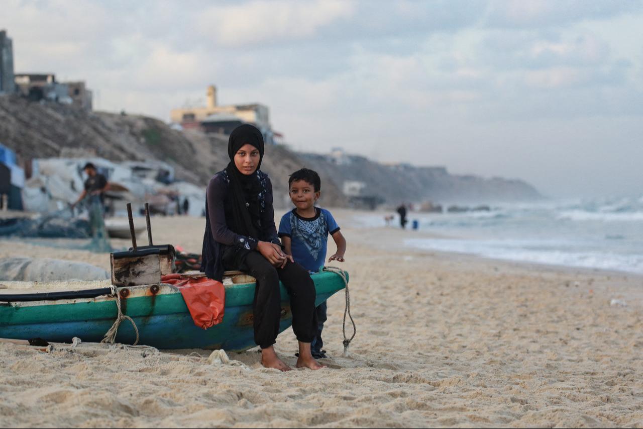 A displaced Palestinian girl and a child sit on a fishing boat along the shore in Deir el-Balah in the central Gaza Strip, on October 5, 2025. (AFP Photo)