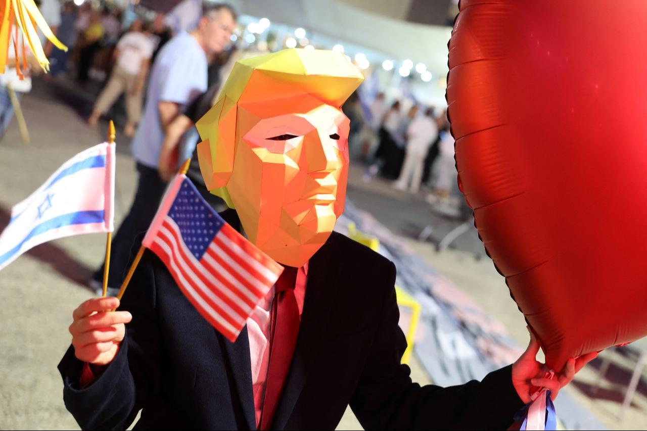A person wearing a mask in the effigy of US President Donald Trump, holds a heart-shaped balloon during a rally in Tel Aviv on October 4, 2025. (AFP Photo)