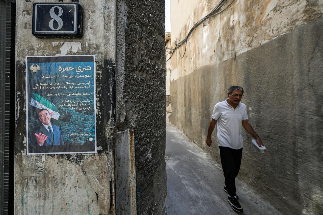 An election poster of Henry Hamra, a Syrian-American parliamentary candidate, displayed on a wall along an alley in Damascus, Oct. 3, 2025. (AFP Photo)