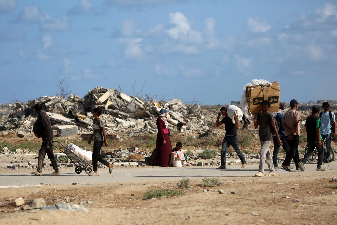 Palestinians carrying bags and empty cardboard boxes walk past a destroyed building as they return from a food distribution point run by the GHF, Gaza Strip, Oct. 5, 2025. (AFP Photo)
