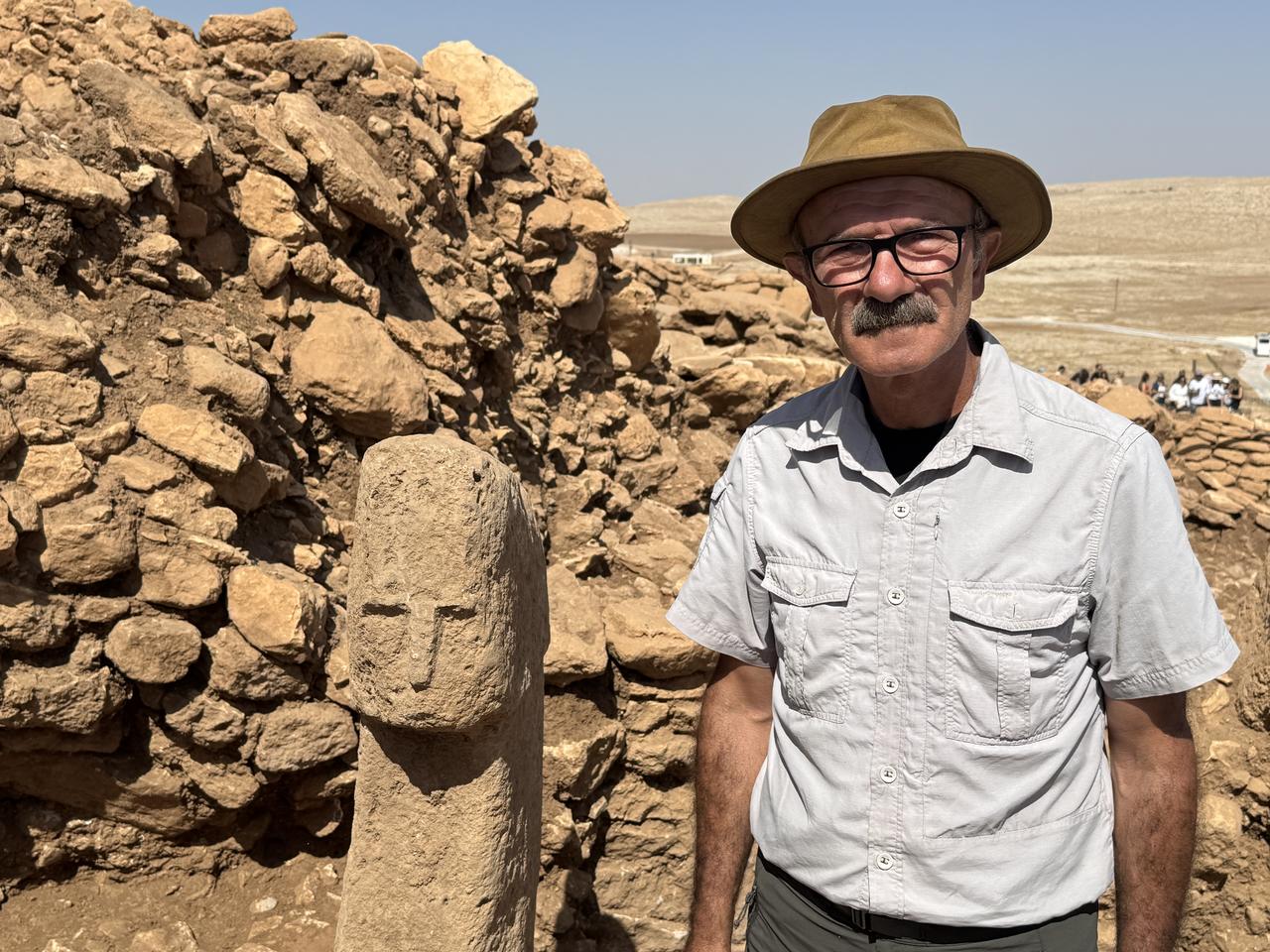 A newly discovered 12,000-year-old pillar carved with a human face stands beside Professor Necmi Karul at the Karahantepe excavation site in Sanliurfa, Türkiye, Oct. 6, 2025. (AA Photo)