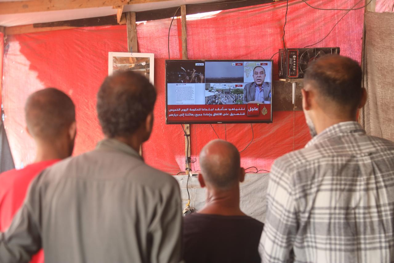 Palestinians follow news about ceasefire agreement that was announced and expected to take effect through television and news channels on their mobile phones in Khan Yunis, Gaza, Oct. 9, 2025. (AA Photo)