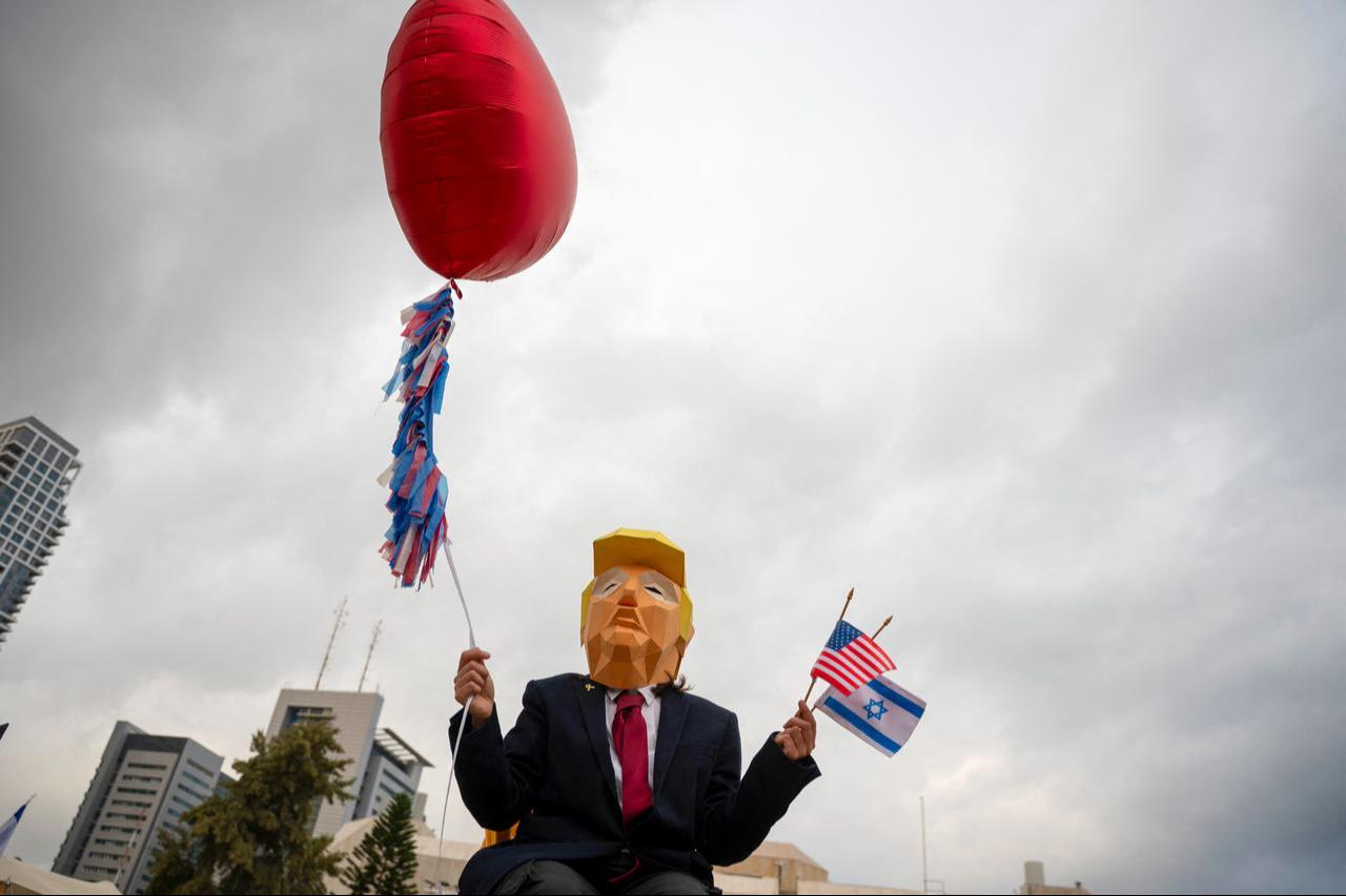 A person wearing a mask depicting US President Donald Trump holds US and Israeli flags after the hostage deal declared by Trump, at Hostage Square in Tel Aviv, Oct. 9, 2025. (AFP Photo)