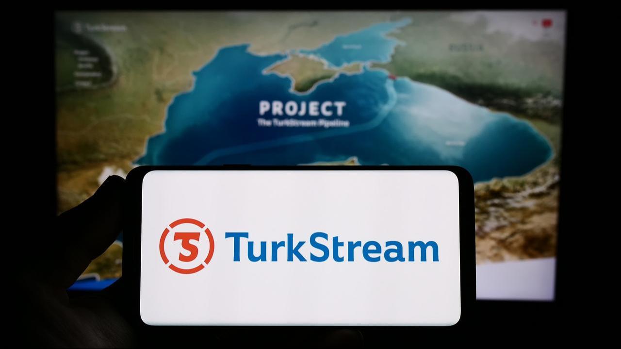 18 Haziran 2023'te Almanya'nın Stuttgart kentindeki web sitesinin önünde, üzerinde TürkAkım doğalgaz boru hattı logosu bulunan akıllı telefon tutan kişi. (Adobe Stok Fotoğrafı)