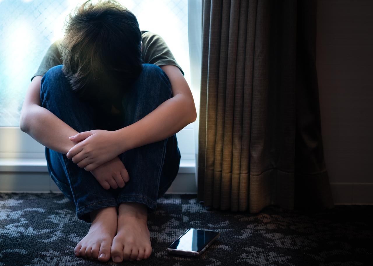 A teenage boy sits alone with his smartphone, symbolizing rising anxiety and depression. (Adobe Stock Photo)