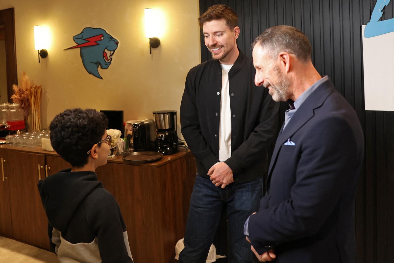 ABD'li YouTuber James Stephen "Jimmy" Genellikle MrBeast (C) olarak tanınan Donaldson, şirketinin CEO'su Jeff Housenbold'un (R) röportaj öncesinde izlediği sırada bir çocukla konuşuyor. "Canavar Ülkesi" 12 Kasım 2025'te Riyad'ın Boulevard City eğlence kompleksindeki geçici eğlence parkı. (AFP Fotoğrafı)