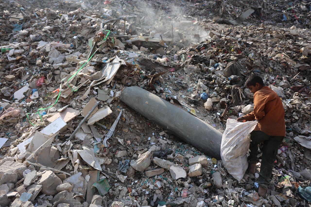 A Palestinian boy collects plastic near an unexploded missile at a rubbish dump in the Firas market area of Gaza City on November 12, 2025. (AFP Photo)