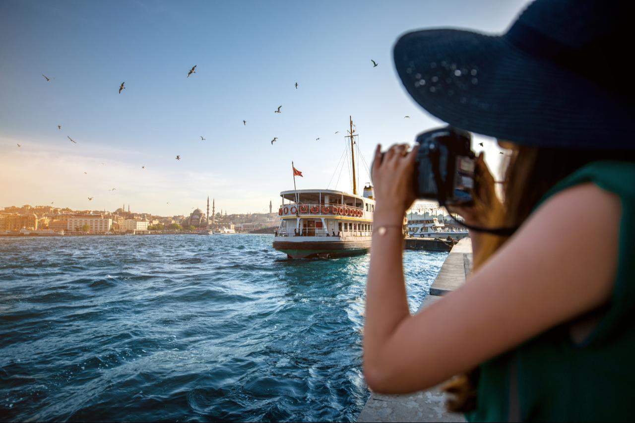 A tourist photographs a ferry crossing the Bosphorus in Istanbul, Türkiye. (Adobe Stock Photo)