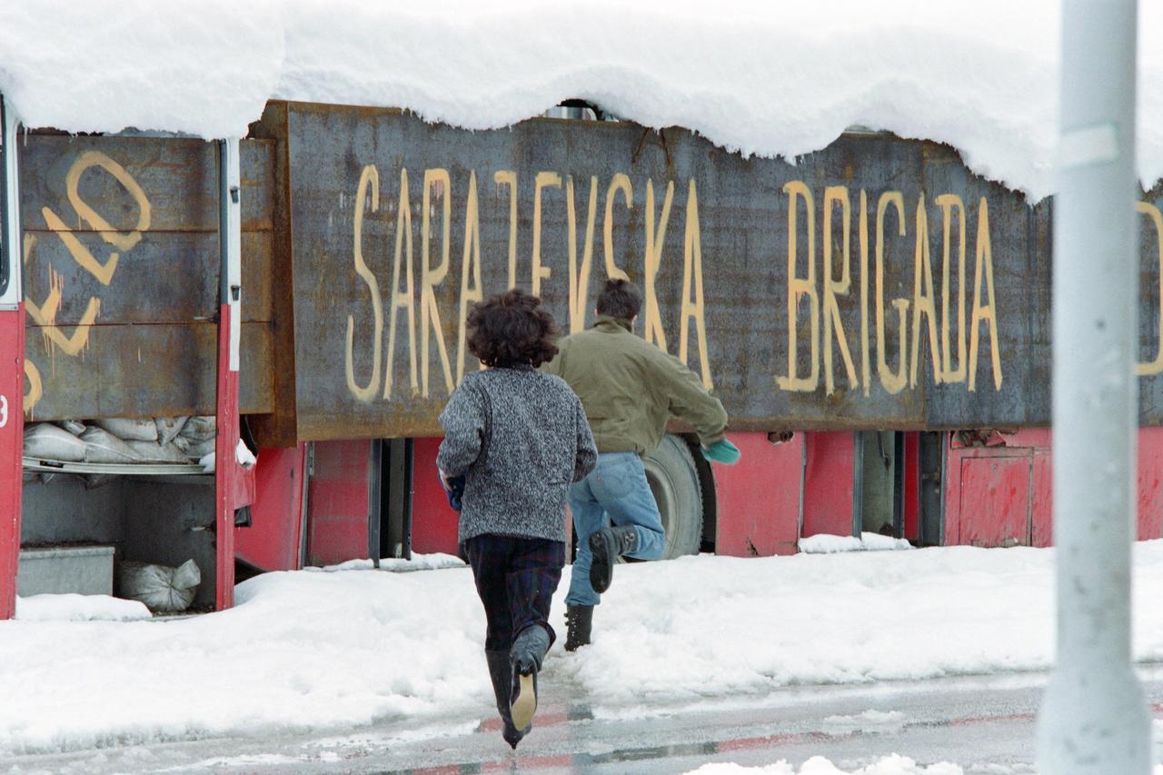 A couple runs to get shelter from snipers behind a bus carrying the legend "Sarajevo brigade", on March 28, 1993 in Sarajevo during the Bosnian war. (AFP File Photo)