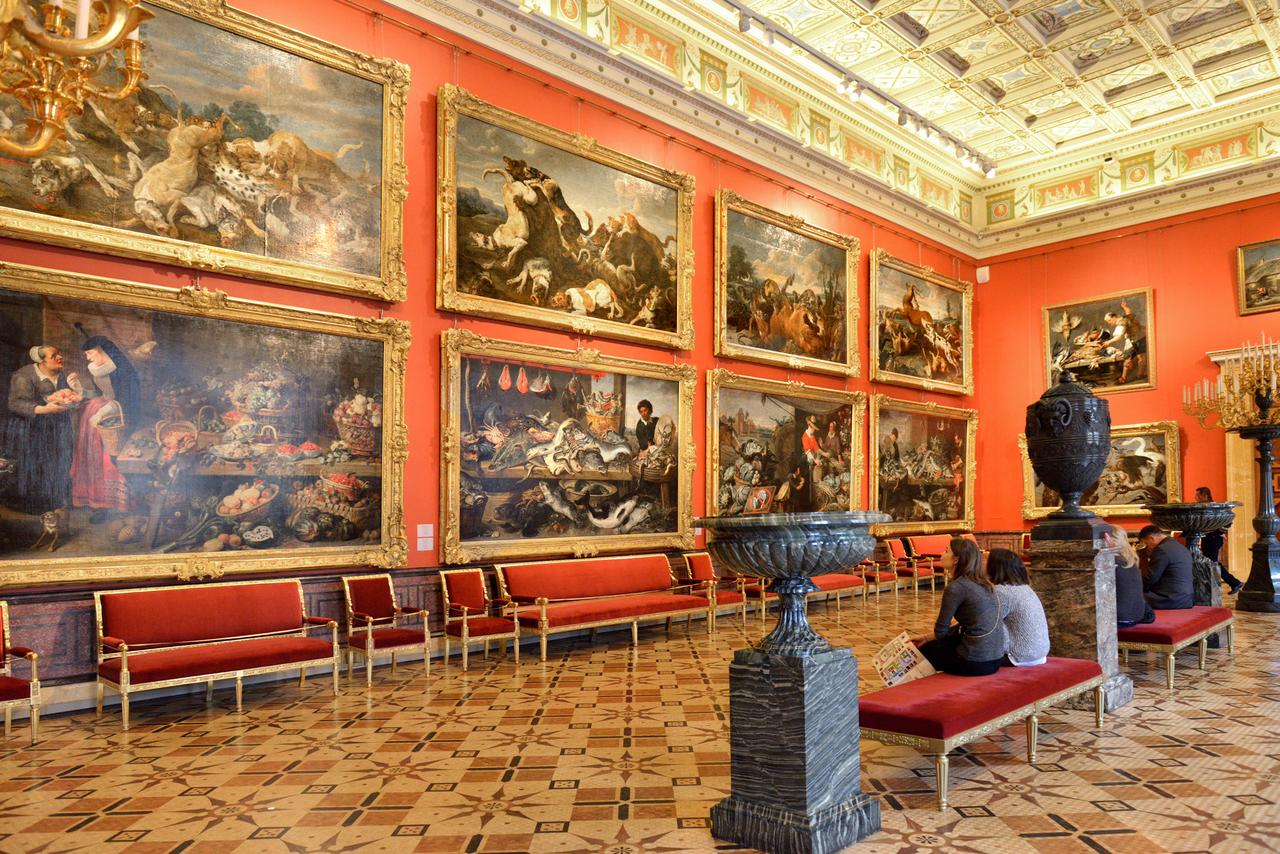 Guests sit on red benches beneath monumental baroque canvases in a richly decorated gallery of the Hermitage Museum, surrounded by marble floors and ornate ceilings. (Adobe Stock Photo)