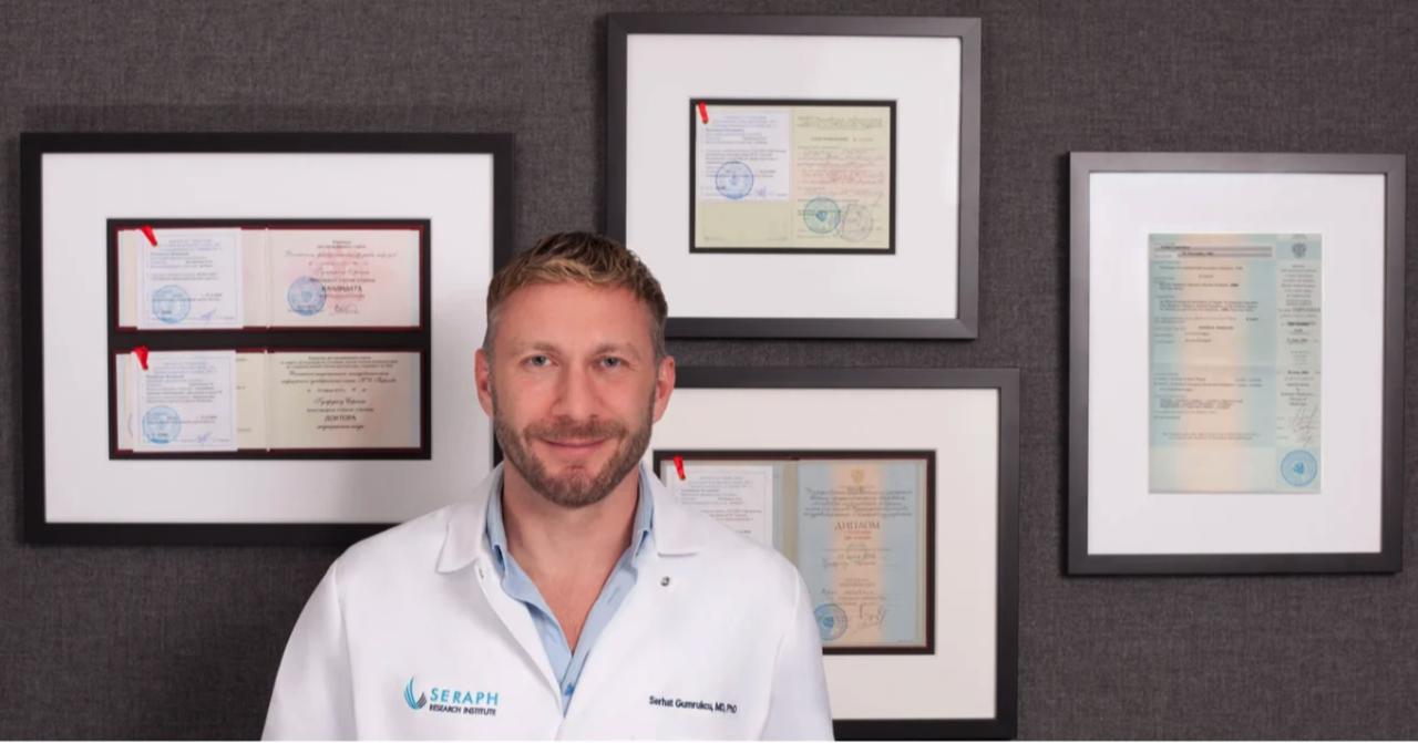Serhat Gumrukcu poses in front of fake Russian medical degrees, shared on the Seraph Research Institute website, 2021, Los Angeles, California. (Image via Seraph Research Institute)