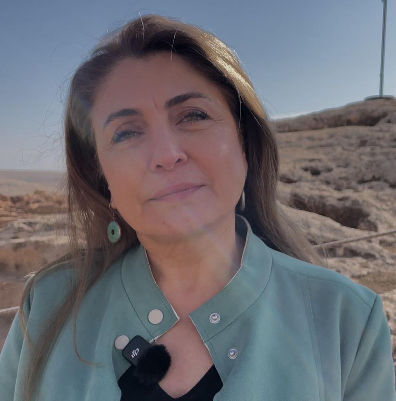 Assoc. Prof. Eylem Ozdogan speaks on camera during a field presentation at the Karahantepe, with the settlement’s rocky landscape visible in the background. (Photo by Koray Erdogan/Türkiye Today)