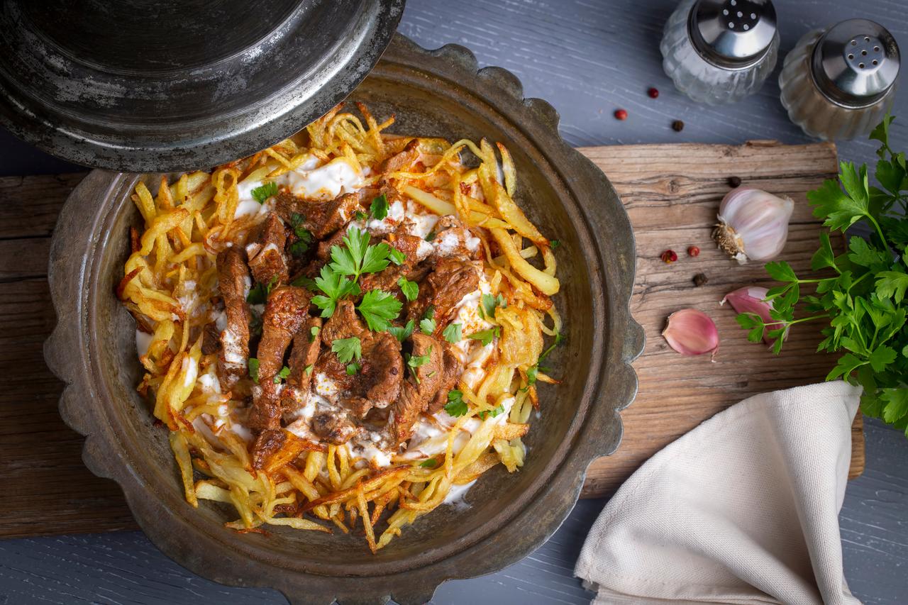 Cokertme kebabi from the Milas–Bodrum region, prepared with thin fried potatoes, marinated meat and garlic yogurt, Türkiye, accessed on November 28, 2025. (Adobe Stock Photo)