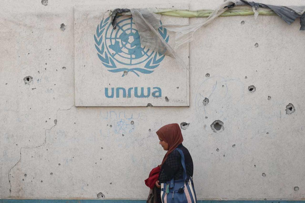 A Palestinian woman walks past a damaged wall bearing the UNRWA logo at a camp for internally displaced people in Rafah in the southern Gaza Strip on May 28, 2024. (AFP Photo)