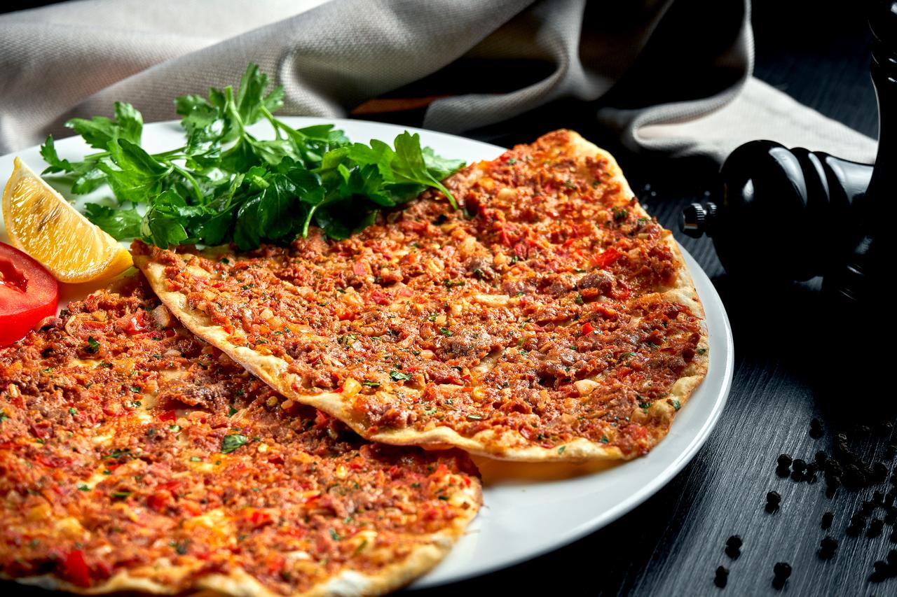 A table setting featuring lahmacun alongside traditional accompaniments such as parsley, onion salad, and lemon, highlighting its place in Türkiye’s everyday cuisine. (Adobe Stock Photo)