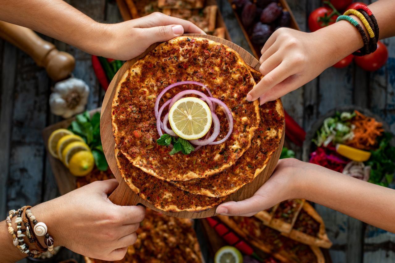 A serving of Gaziantep-style lahmacun, a thin flatbread topped with seasoned minced meat, garnished with sliced onion and lemon. (Adobe Stock Photo)