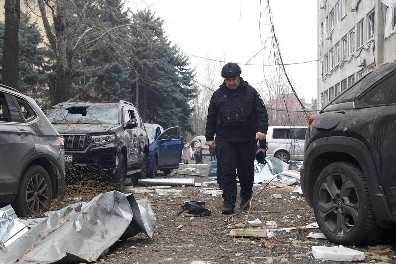A Ukrainian law enforcement officer walks past damaged cars at the site of an air attack in Dnipro on December 1, 2025. (AFP Photo)