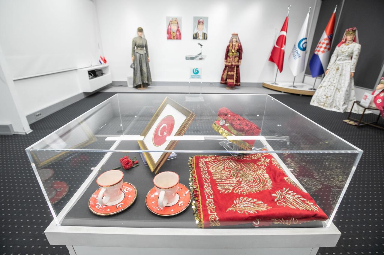 Traditional wedding objects, including Turkish coffee cups, a red embroidered cloth and a framed Turkish flag, are seen in a display case at the exhibition at the Yunus Emre Institute in Zagreb, Croatia, Dec. 11, 2025. (AA Photo)