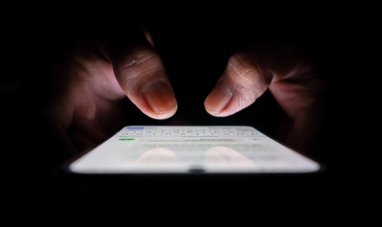 Hands using a smartphone in the dark, symbolizing the unseen risks and lasting digital footprint created by online sharing. (Adobe Stock Photo)