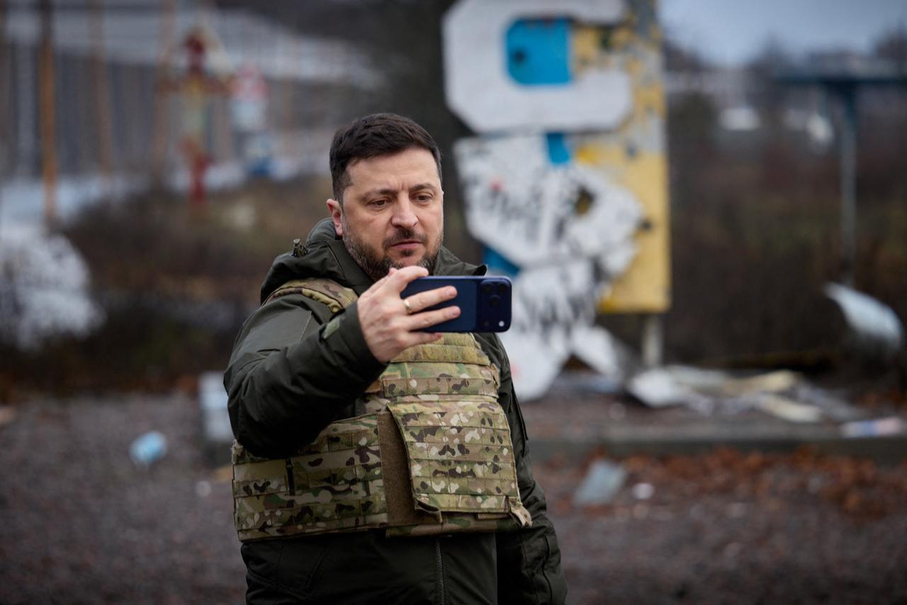 Ukraine's President Volodymyr Zelenskyy records a video message on his mobile phone in front of the road sign marking the entrance to Kupiansk, Kharkiv region, Dec. 12, 2025. (AFP Photo / Ukrainian Presidential Press Service)