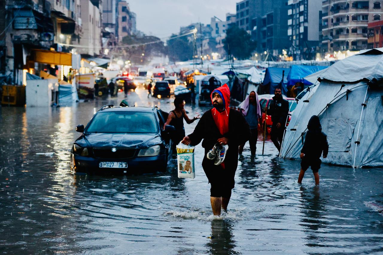Displaced Palestinians walk through floodwaters following heavy rains in Gaza City on December 15, 2025. ( AFP Photo )