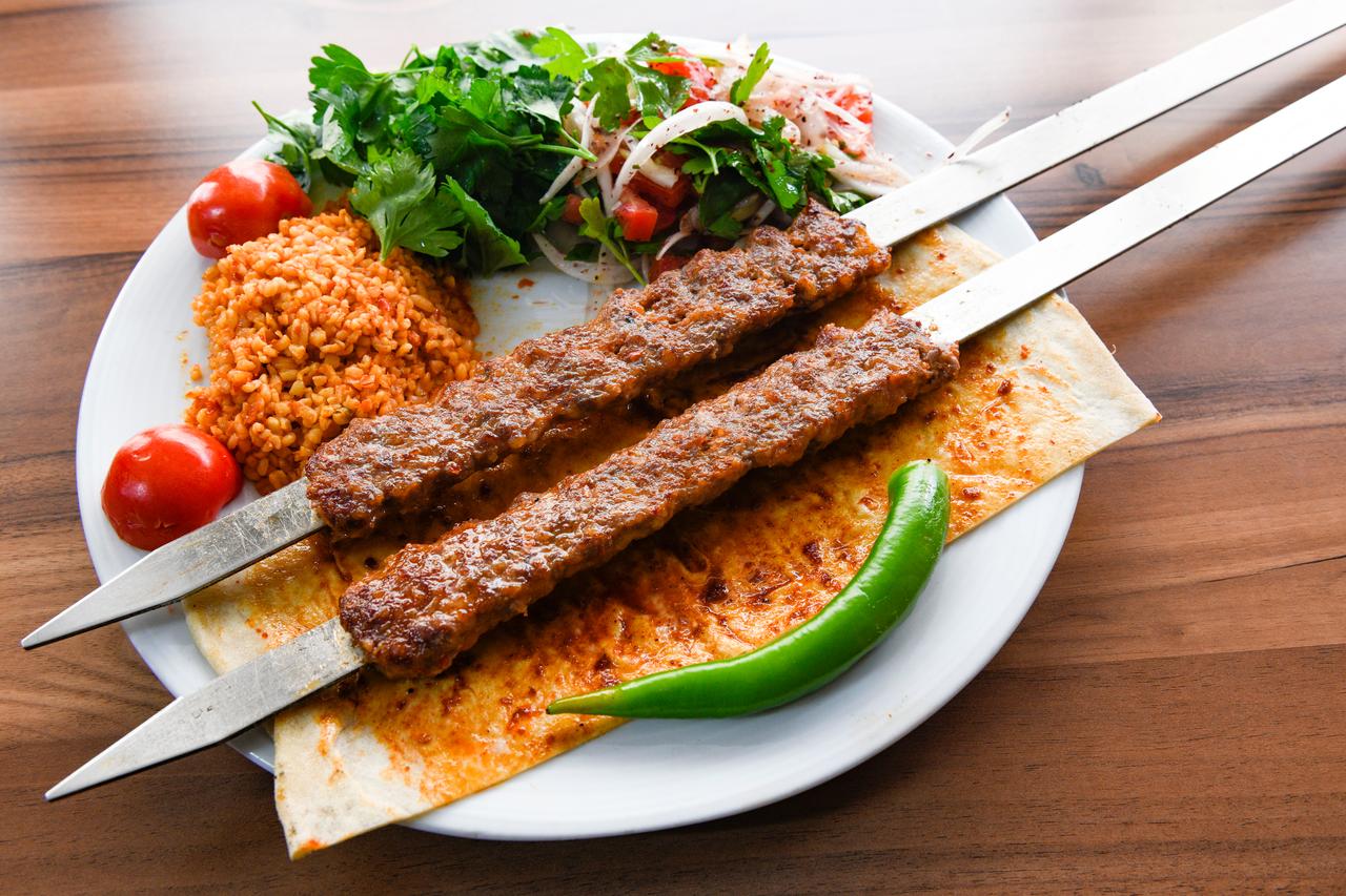 Plate of grilled kebab served with vegetables, onions and rice. (Adobe Stock Photo)