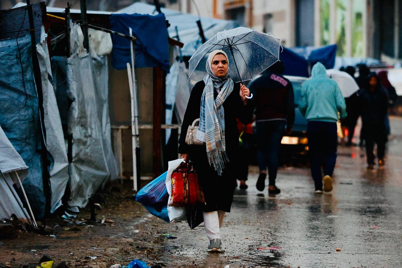 A displaced Palestinian woman holds an umbrella to shield from the rain in Gaza City on December 15, 2025. ( AFP Photo )