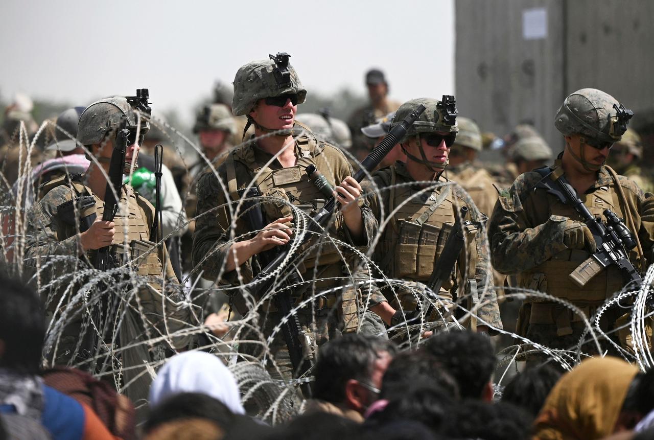 US soldiers stand guard behind barbed wire as Afghans sit on a roadside near the military part of the airport in Kabul, Afghanistan, on August 20, during the lead up to the complete withdrawal of US forces from Afghanistan. (AFP Photo)