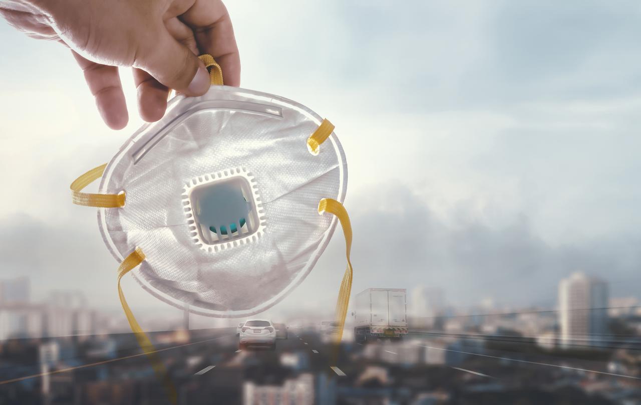 A person holding face mask in a city covered by smog. Fine particles in the air, called PM2.5, are smaller than 2.5 micrometers and can be harmful when breathed in. (Adobe Stock Photo)