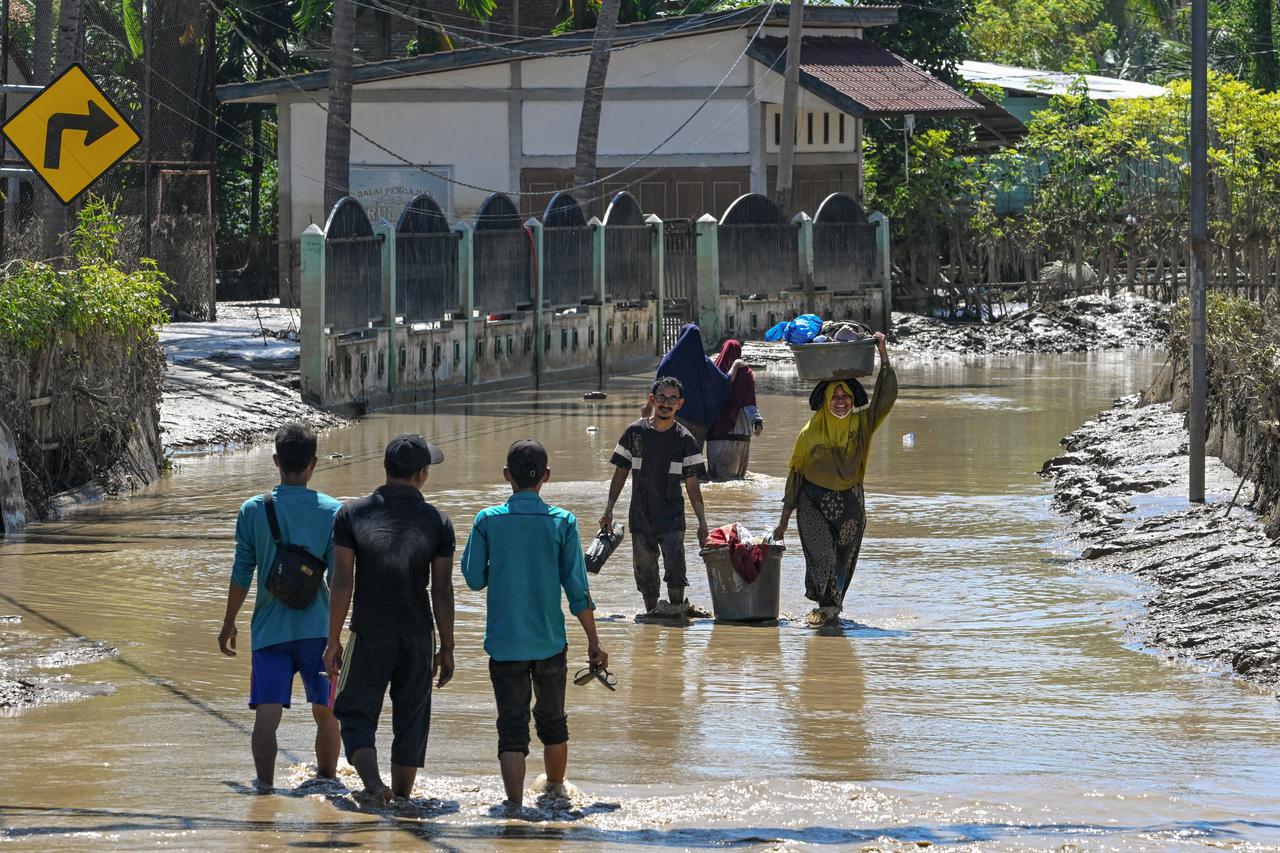 People walk through the mud carrying their belongings after flash floods in Meureudu, Pidie Jaya, Aceh province, Indonesia. November 30, 2025. (AFP Photo)