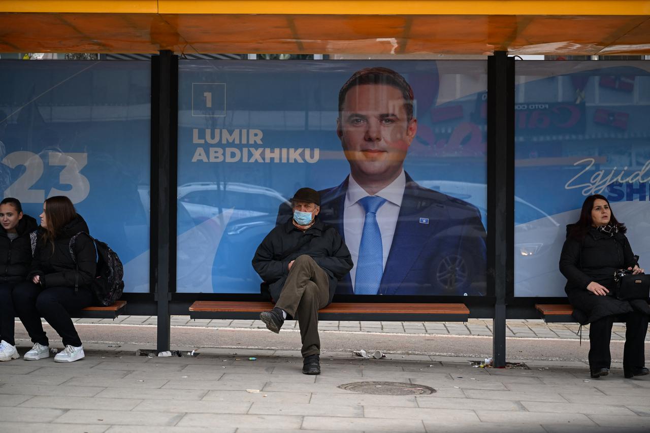 Commuters sit on a bench at a bus stop as an election poster of Lumir Abdixhiku, leader of the Democratic League of Kosovo (LDK) party, is displayed in Pristina on Dec. 21, 2025. (AFP Photo)