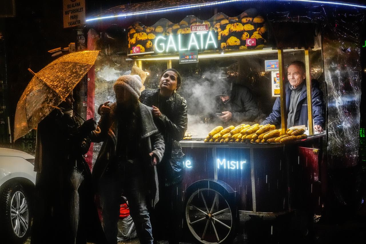 People shelter under umbrellas near a street food vendor as sleet falls in the Beyoglu Taksim district of Istanbul on Dec. 30, 2025. (AA Photo)