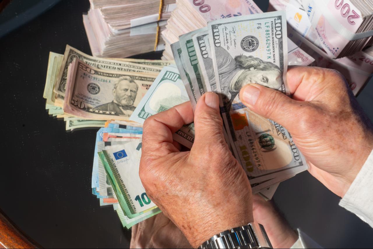 A person counts US dollar banknotes alongside stacks of Turkish lira and euro bills. (Adobe Stock Photo)