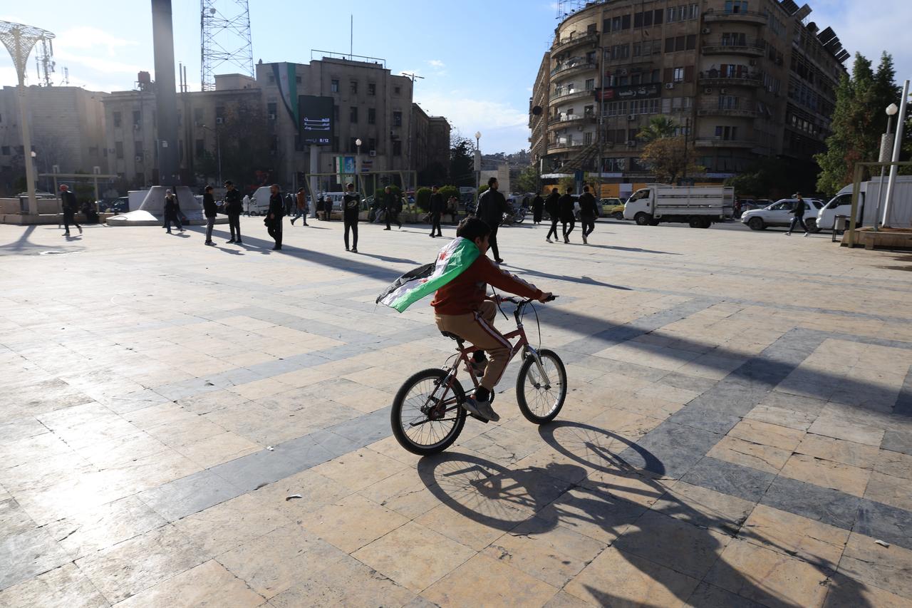 A boy rides a bicycle with a Syrian flag on his shoulder while daily life continues after 14 years of civil war and the fall of the 61-year Baath regime as Syrians are looking to the future with hope on Dec. 1, 2025 in Aleppo, Syria. (AA Photo)