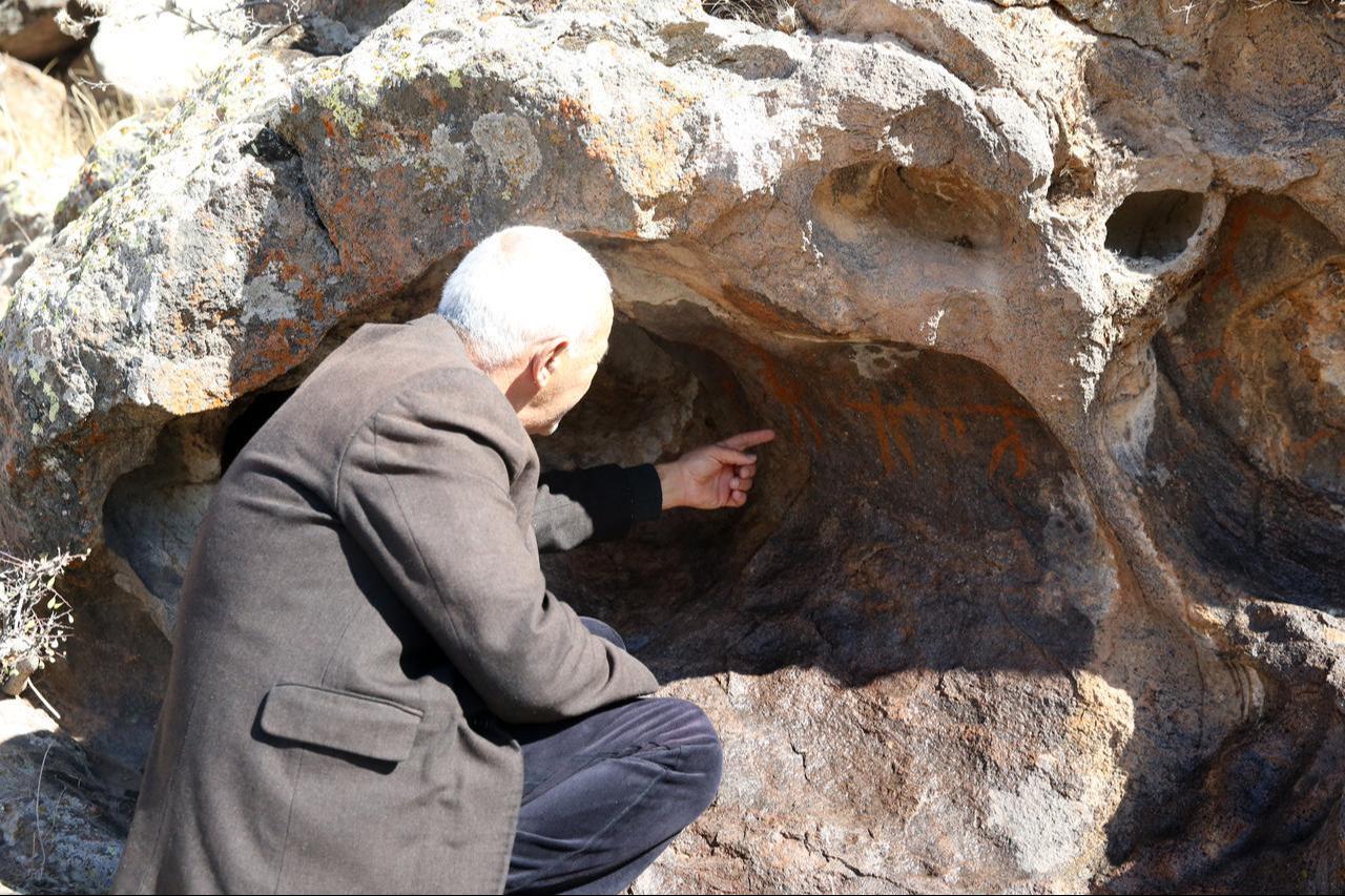 Professor Osman Ozsoy points at rock paintings with human figures thought to date back to the Neolithic Age on a rocky slope in Kayseri, Türkiye, Nov. 19, 2025. (AA Photo)