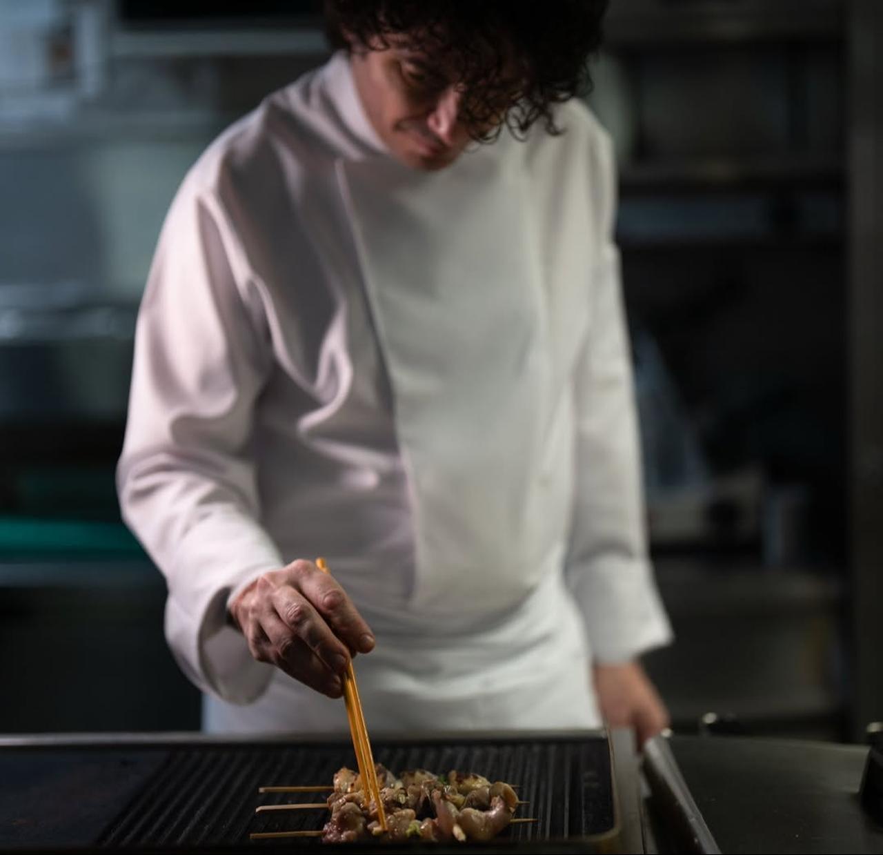 Chef Sinan Damgacioglu grills skewered meat over a hot griddle during service in a professional kitchen, Nov. 6, 2025. (Photo via Instagram/@sinandamgacioglu)