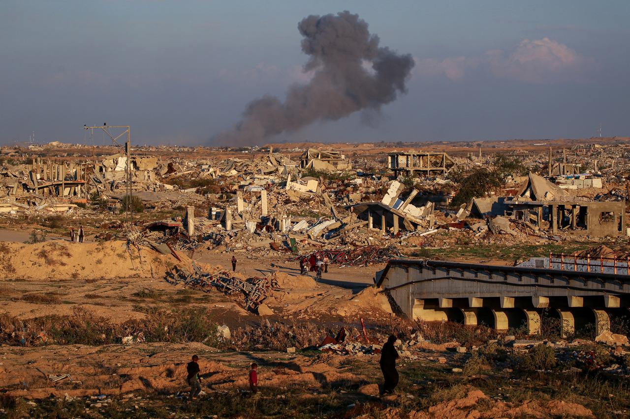 People walk amid the rubble of destroyed buildings at the Nuseirat camp for displaced Palestinians as smoke billows in the distance following Israeli strikes, Dec. 2, 2025. (AFP Photo)