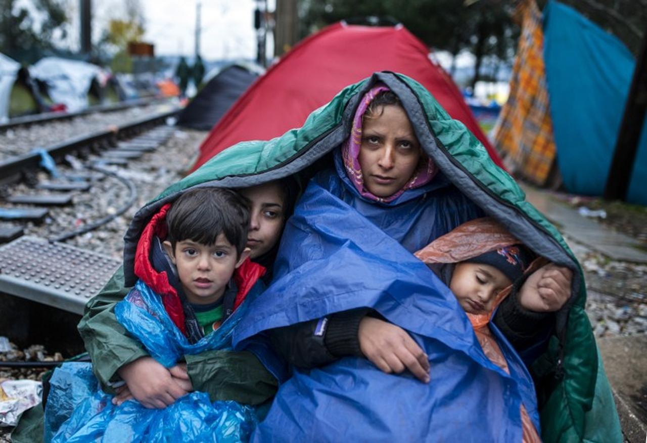 A woman and her children look on as migrants and refugees wait to cross the Greece-Macedonia border in the rain on November 27, 2015 near Gevgelija. (AFP Photo)