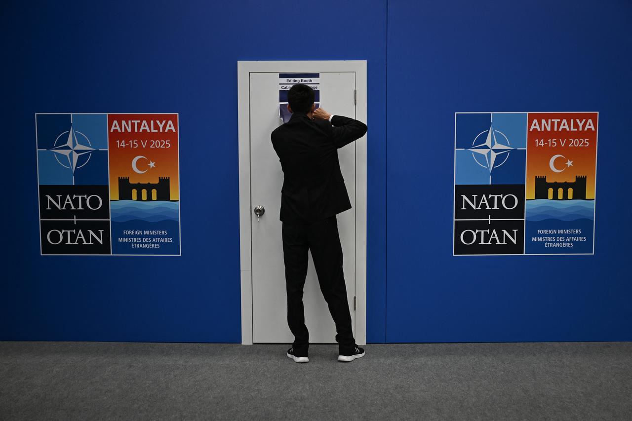 A staff sticks a poster next to placards announcing the informal meeting of NATO Ministers of Foreign Affairs, at the NEST Convention Center in Antalya on May 14, 2025. Foreign ministers from NATO countries gather in the Turkish coastal city of Antalya where they are expected to discuss ramping up defence spending, hours before the Russia-Ukraine talks are supposed to get underway. (Photo by Ozan KOSE / AFP)