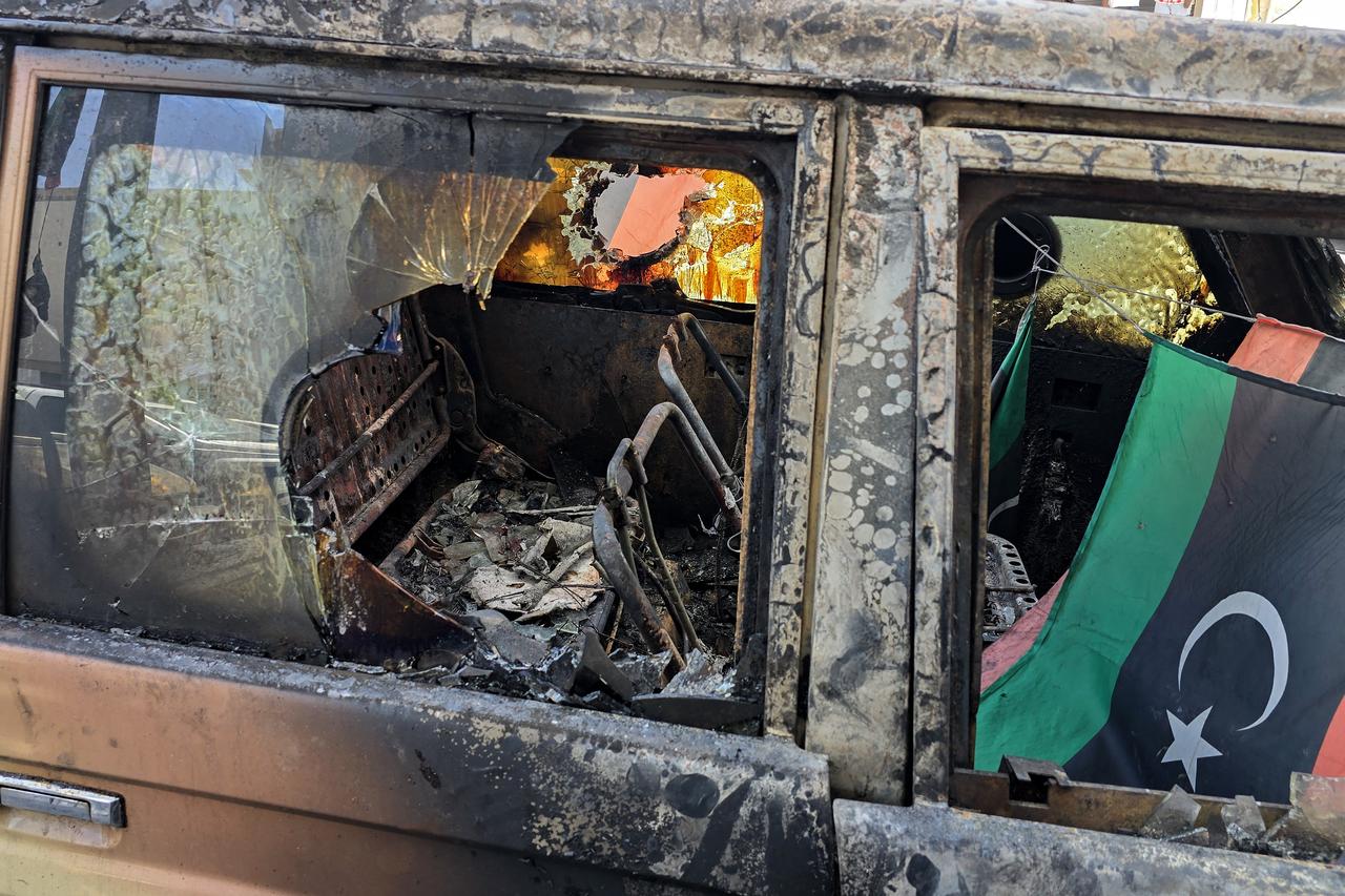 A Libyan flag flutters on a destroyed car following overnight clashes in the southern district of Abu Salim in the capital Tripoli on May 13, 2025. Overnight clashes in Libyas capital killed at least six people, an emergency medical service said on May 13, with local media reporting that an armed group leader was among the dead. (Photo by Mahmud Turkia / AFP)