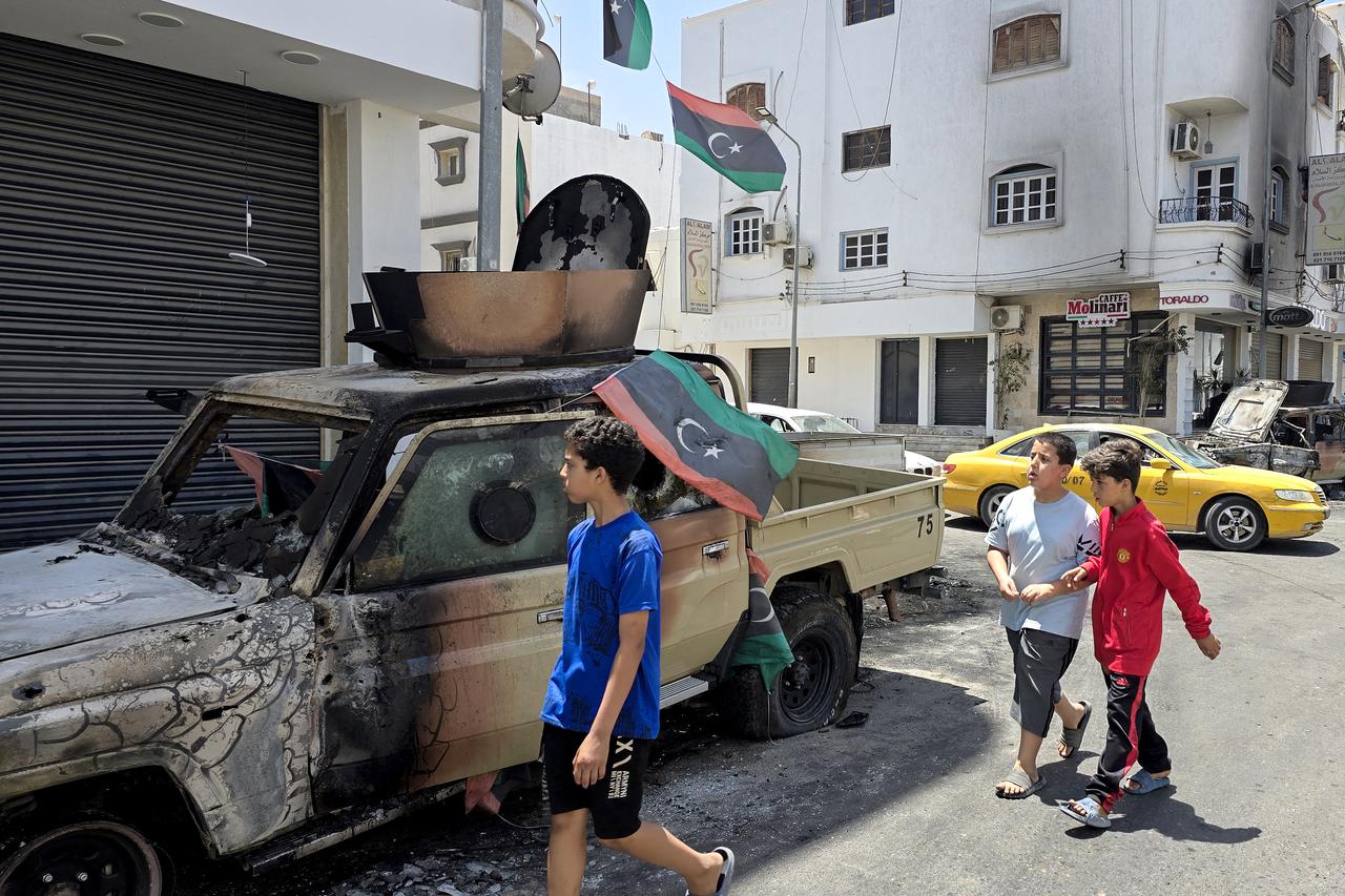 A Libyan flag flutters on a destroyed car as children walk past following overnight clashes in the southern district of Abu Salim in the capital Tripoli on May 13, 2025. Overnight clashes in Libyas capital killed at least six people, an emergency medical service said on May 13, with local media reporting that an armed group leader was among the dead. (Photo by Mahmud Turkia / AFP)