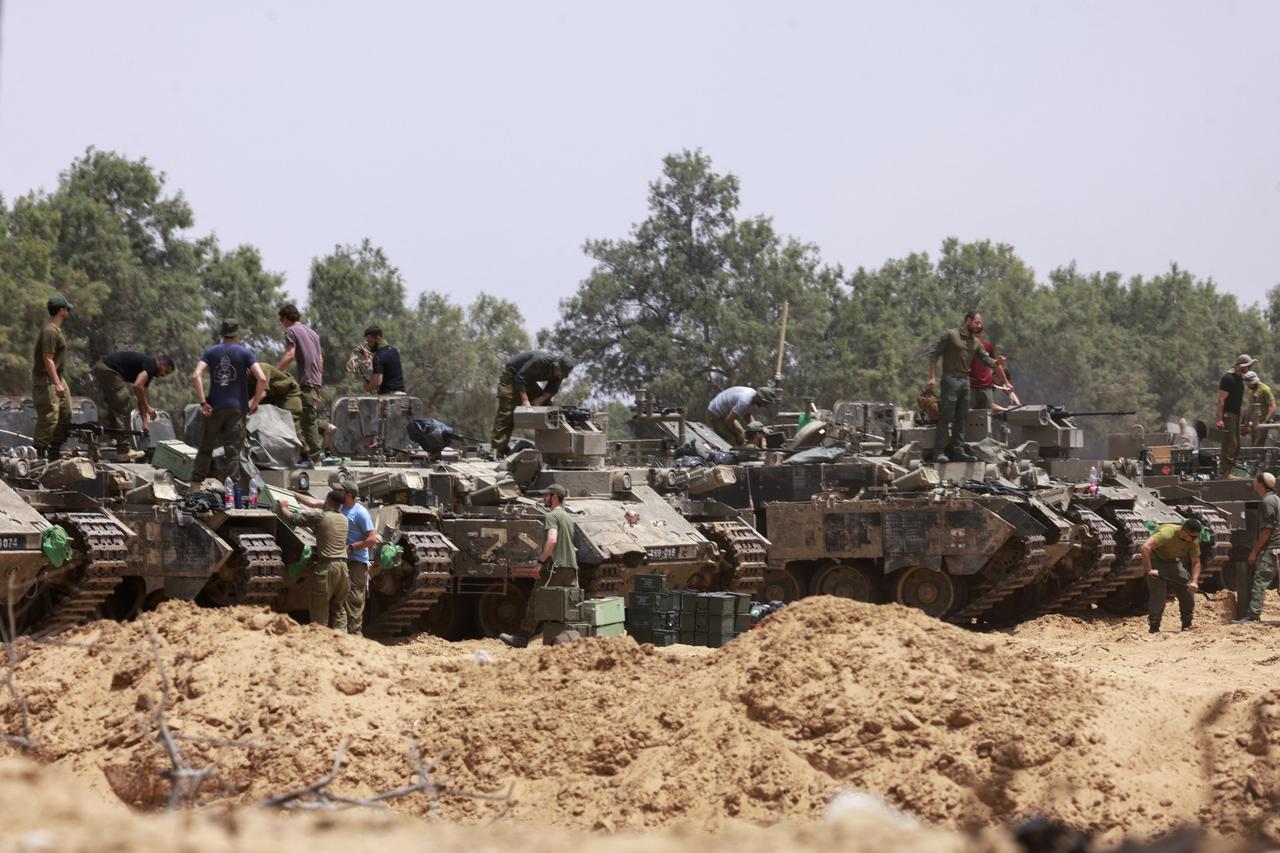 Israeli troops work on their armoured vehicles at a position by Israels border with the Gaza Strip on May 18, 2025. Israels military has announced a day earlier the expansion of its operations, saying it is aimed at  achieving all the wars objectives  including releasing hostages and  the defeat of Hamas , the Palestinian movement that runs Gaza. (Photo by Menahem KAHANA / AFP)