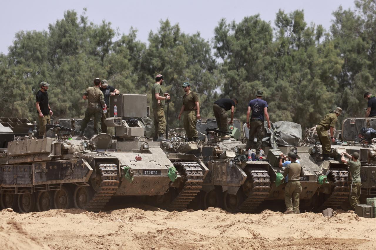 Israeli troops work on their armoured vehicles at a position by Israels border with the Gaza Strip on May 18, 2025. Israels military has announced a day earlier the expansion of its operations, saying it is aimed at  achieving all the wars objectives  including releasing hostages and  the defeat of Hamas , the Palestinian movement that runs Gaza. (Photo by Menahem KAHANA / AFP)