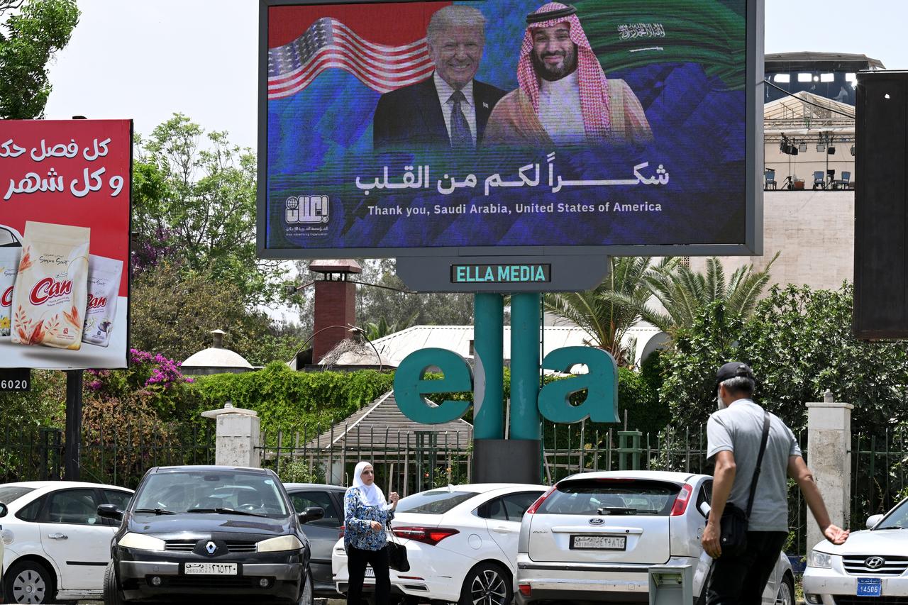 People walk past a billboard displaying portraits of Saudi Crown Prince Mohammed bin Salman and US President Donald Trump with a slogan thanking Saudi Arabia and the United States, in Damascus on May 14, 2025. (AFP Photo)