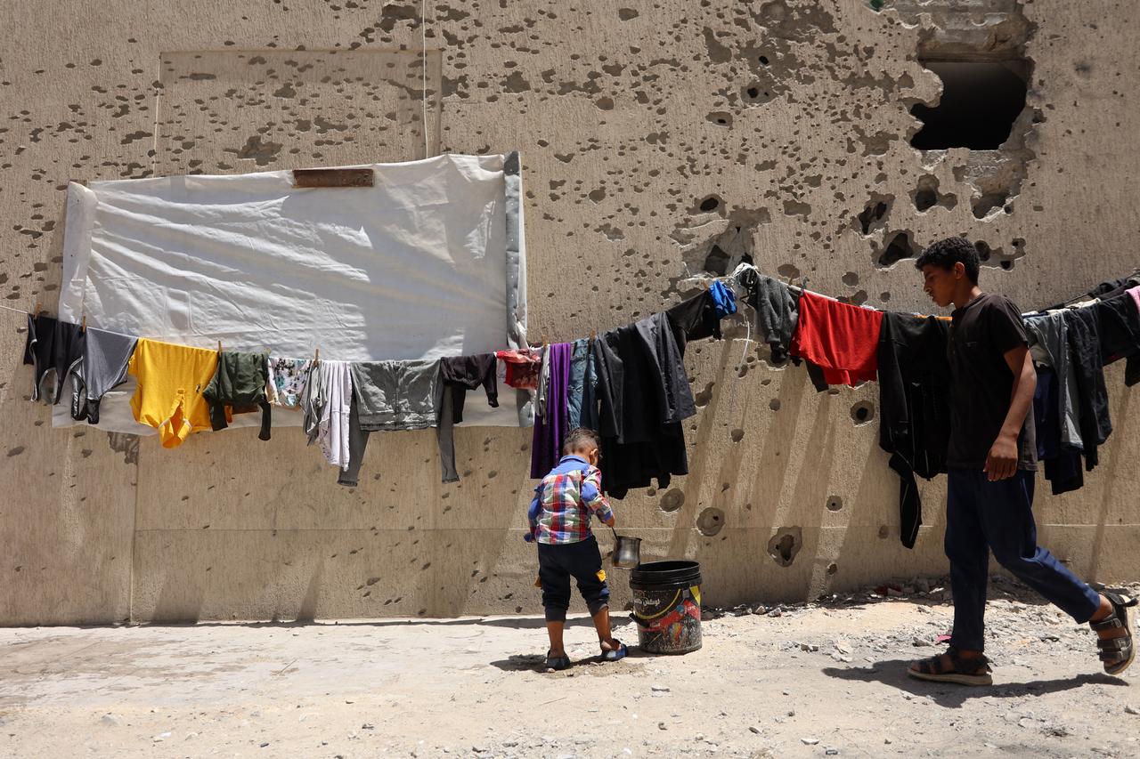 A Palestinian boy stands under a line of laundry drying against a shrapnel-riddled wall in Gaza City on May 25, 2025. Rescuers in Gaza said eight people were killed and dozens more wounded in Israeli air strikes across the Palestinian territory on May 25. (Photo by Omar AL-QATTAA / AFP)