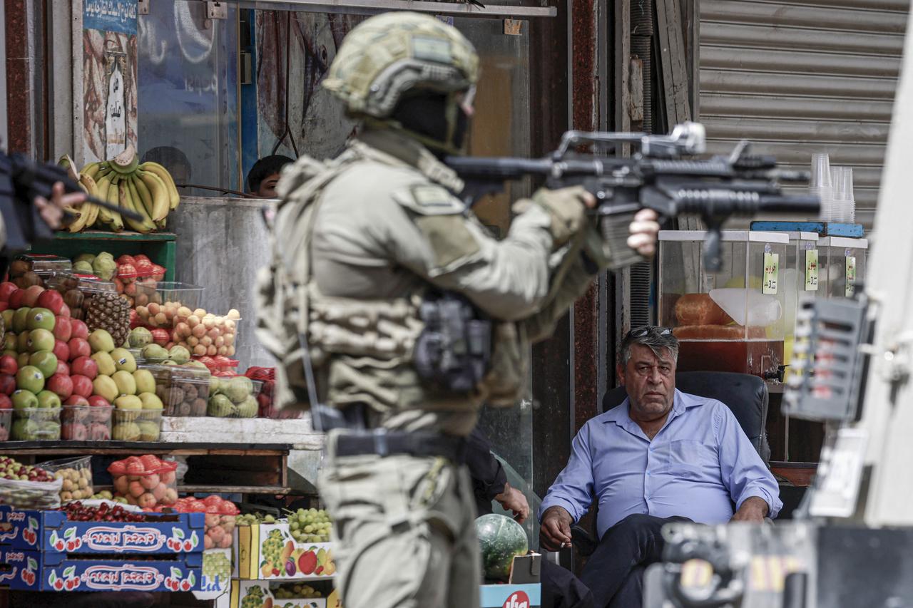 An Israeli army soldier aims his rifle as a Palestinian man looks on during a raid in the heart of the Palestinian city of Nablus, in the occupied West Bank on May 27, 2025. Israeli forces Tuesday raided foreign exchange stores in several West Bank cities including Ramallah and Nablus, accusing their parent company of  connections with terrorist organisations , per an army closure notice. (Photo by Jaafar ASHTIYEH / AFP)